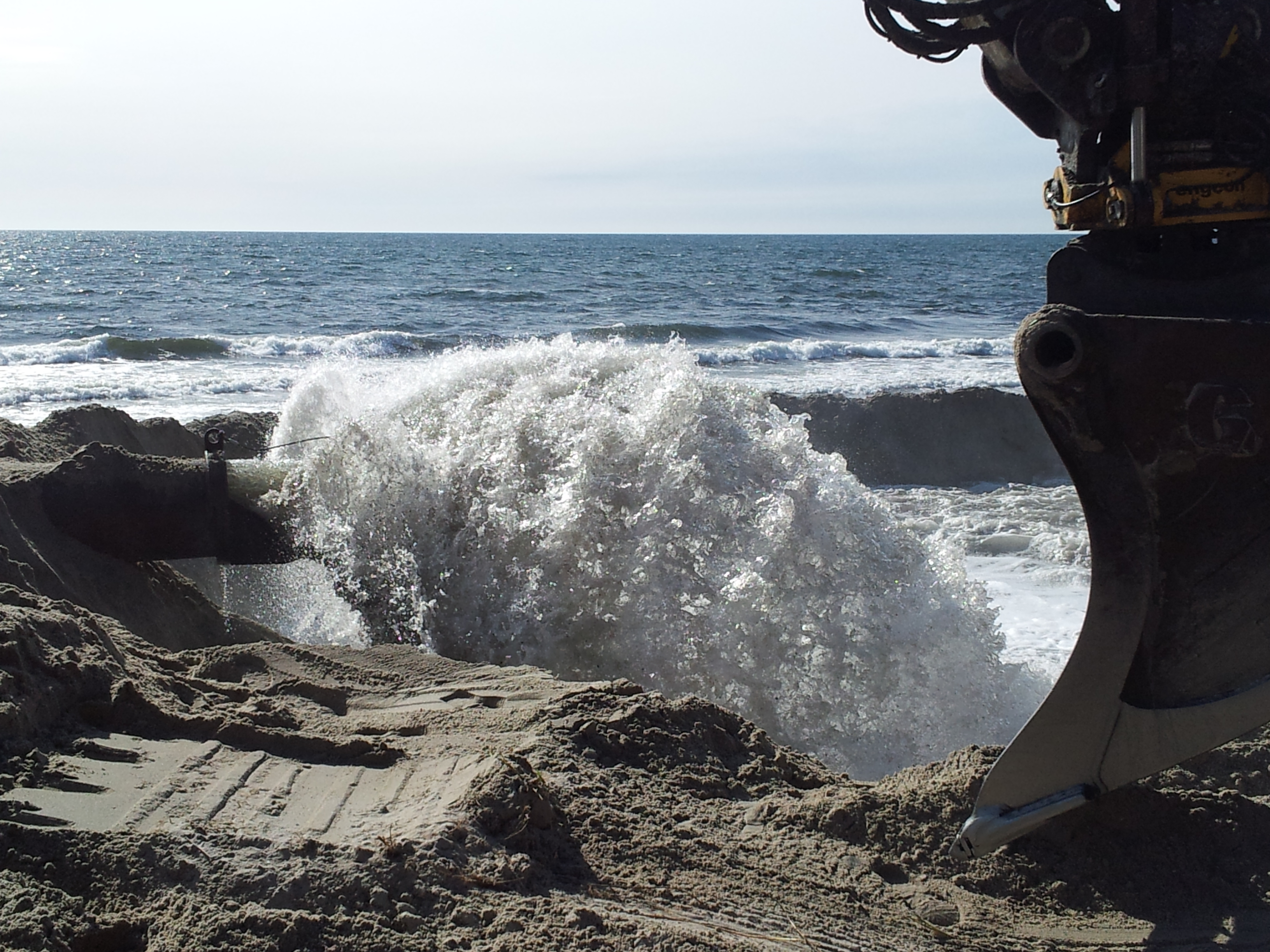 Sand och vatten sprutar ut ur en rörledning på stranden