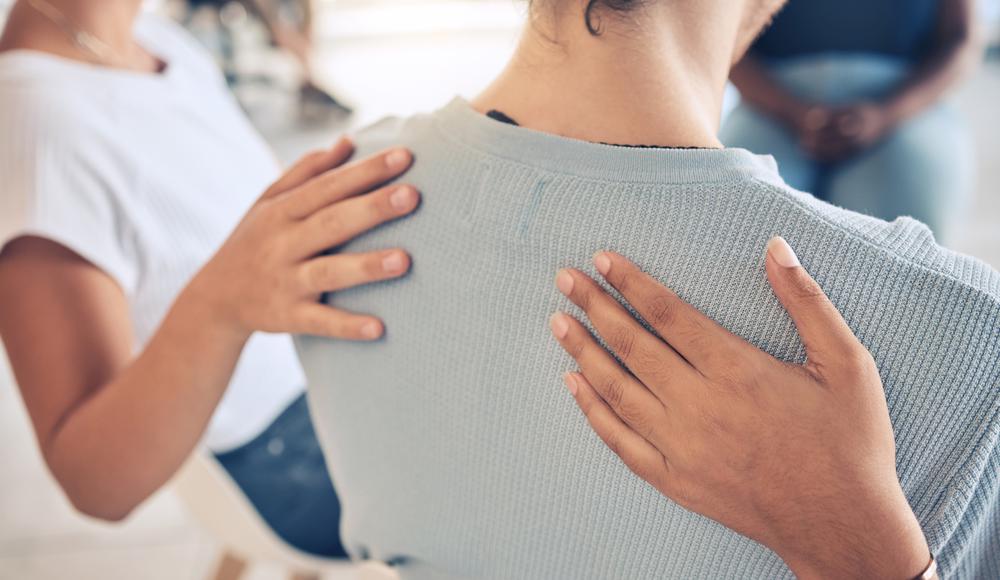 Två personer håller sina händer på baksidan av en tredje persons axel